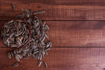Heap of sunflower seeds in bowl on brown wooden table. Top view, copy space. Food, harvest,...