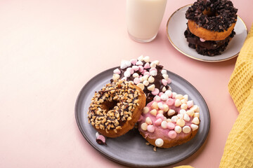 Donuts with icing on plate on pastel pink background.