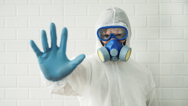 Medical Healthcare Biology Wearing Medical Mask With Safety Glasses And In White Protective Suit. Showing Stop And No Sign Gesture