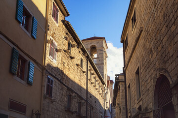 Fototapeta na wymiar Light and shadow, narrow street of ancient Mediterranean town on sunny winter day. Montenegro. Old Town of Kotor, UNESCO-World Heritage Site. View of St. Francis Monastery Tower