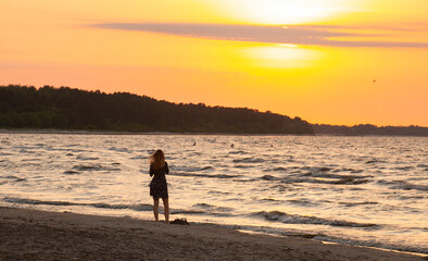 Naklejka premium Lonely girl admires the sunset on the sea, sandy beach.