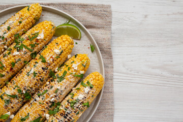 Homemade Elote Mexican Street Corn on a plate on a white wooden surface, top view. Flat lay, overhead, from above. Copy space.