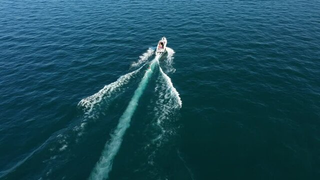 Tubing boat with people moving behind the boat on the water. Aerial view of motor speed boat pulls Green inflatable rubber raft with people. 360 ° turn of the boat