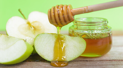 The Jewish holiday concept, Apple Rosh Hashanah dessert day, on the photo have honey in a jar and drop honey on green apples were sliced on wooden with green background