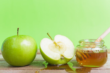 The Jewish holiday concept, Apple Rosh Hashanah dessert day, on the photo have honey in a jar and drop honey on green apples were sliced on wooden with green background