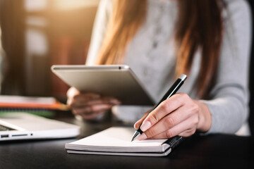 Female businessman use a tablet and take notes in the notebook at the office desk in the morning.