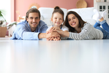 Young Caucasian family with small daughter pose relax on floor in living room, smiling little girl kid hug embrace parents, show love and gratitude, rest at home together.