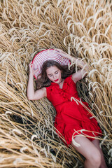 Beautiful girl in red dress and striped hat posing in a wheat field