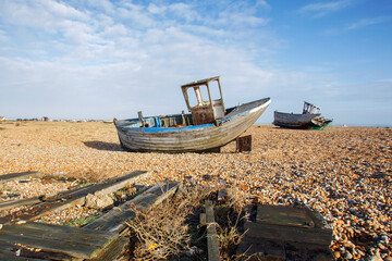 Fototapeta premium Two abandoned fishing boats on the shingle beach at Dungeness with scattered debris - the area has such low rainfall as to qualify as the only desert in the UK.