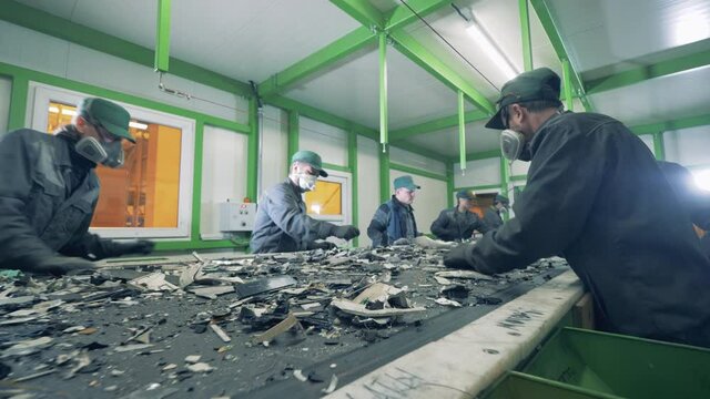 Recycling center workers sort trash on a conveyor.