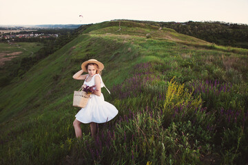 Portrait of beautiful blonde girl in straw hat and with bouquet of wildflowers in straw bag.