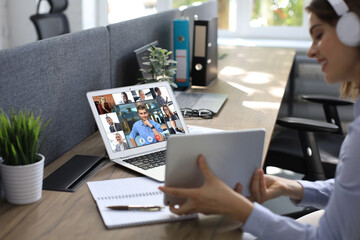 Businesswoman in headphones talking to her colleagues in video conference. Multiethnic business team working from office using laptop, discussing financial report of their company.