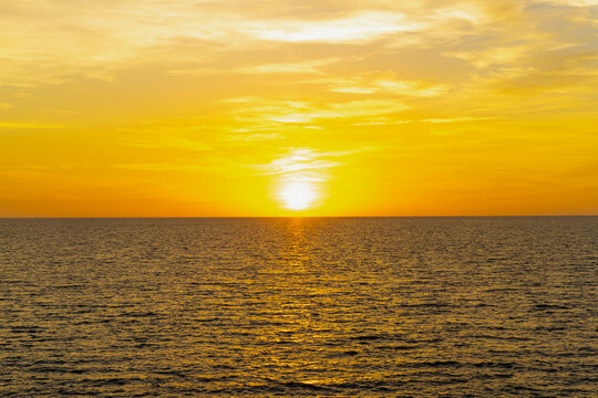 Front view in the blue ocean in the evening, the sun was setting, reflections fell on the smooth calm surface with golden warm light. The sky is clear and clean. Feeling refreshed and relaxed.