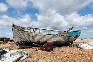 Abandoned fishing boat on the shingle beach at Dungeness with scattered debris - this area has such...