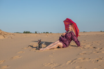 Young woman with long blondy hair wearing a raincoat with umbrella in a desert 