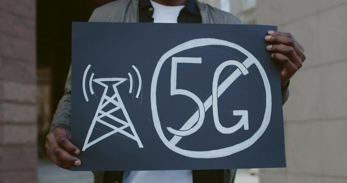 Close up of male hands holding placard with no 5g sign. African american guy doing single protest against new technology and compatible antenna deployment while standing at street
