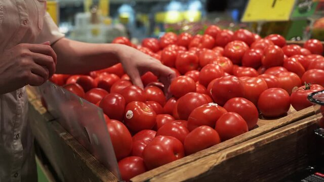 A female hand chooses red tomatoes at the market. counter with tomatoes and other vegetables at the grocery store.