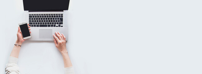 スマートフォンを片手にラップトップを操作する女性