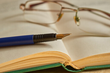 Glasses and a blue fountain pen lie on an open book