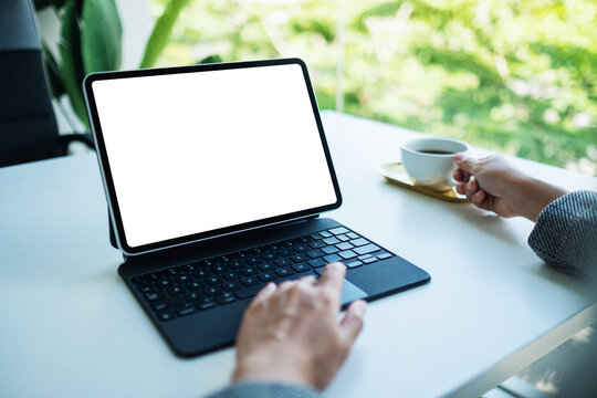 Mockup image of a woman touching on tablet touchpad with blank white desktop screen as computer pc while drinking coffee