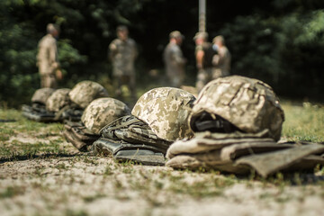 Military helmets and bulletproof vests are lined up on the grass.