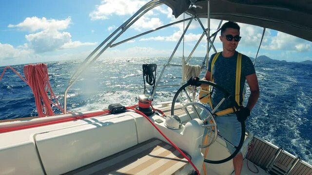 A man is ruling the yacht across the blue ocean waters