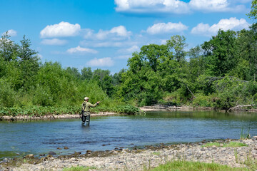 Fototapeta na wymiar A man is fishing with fly fishing in the river on a summer day.