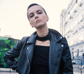  Serious rebel informal teenage girl with bald hair and piercing in urban outdoor city background....