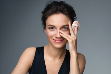 Beautiful woman applying dry powder, using cosmetic cushion on her facial skin. Photo of woman with perfect makeup on gray background. Beauty concept