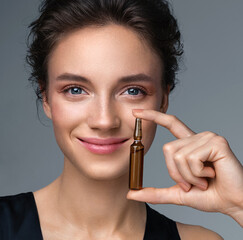 Woman holds ampoule with serum for hair or skin care. Photo of attractive woman with perfect makeup...