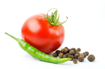 Closeup of black peppercorns, green fresh chili pepper and ripe tomato on the white background