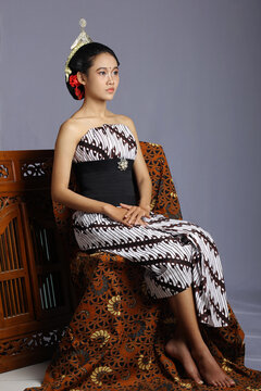 Beautiful javanese woman wearing a lurik. Traditional javanese costume. Woman sitting on a chair with a jarik as a pedestal with a gray background