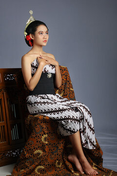 Beautiful javanese woman wearing a lurik. Traditional javanese costume. Woman sitting on a chair with a jarik as a pedestal with a gray background