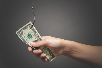 Human hand is holding a dollar on the fishing hook close up on gray background.