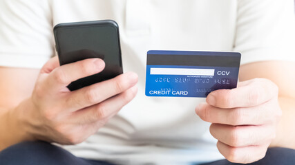 Selective focus at men hand holding credit card while type payment information into smartphone. Online purchase transaction during social distance period.