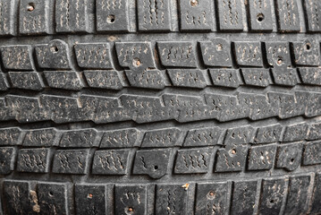 Worn out tread on studded tires of car background.