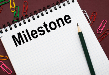 Design concept - Top view of white spiral notebook and pencil with text MILESTONE isolated on red background for mockup