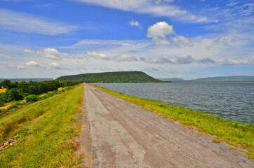 Long old road on the dam of reservoir with green mountain under beautiful sky