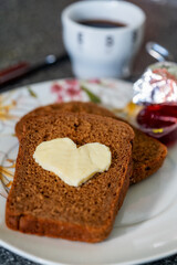 Fototapeta na wymiar Heart shaped butter with jam on a slice of bread next to a cup of coffee