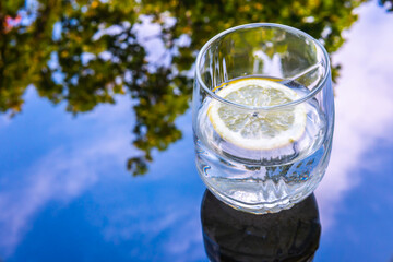 Glass with water and lemon against the background of the reflected sky. Heat