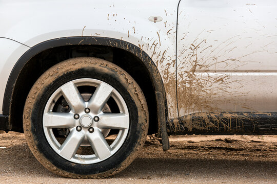 The front wheel of a dirty car in the sand spattered the fender and driver's door with mud.