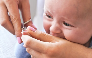 Infant baby boy having his nails cut by mother, detail on scissors and fingertips