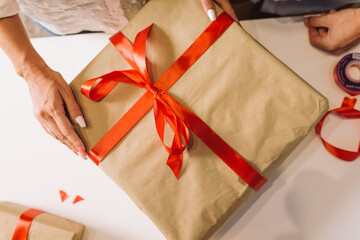Woman`s hands wrapping christmas holiday present with red ribbon.