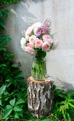Fototapeta na wymiar A romantic photo with a bouquet of delicate pink English roses standing in a vase on a birch tree stump. Romantic bouquet on the background of a concrete wall entwined with virginia creeper.
