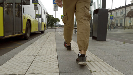 Obraz premium Back view of a man in yellow shirt walking along the bus stop sitting on a bench. Waiting for a bus