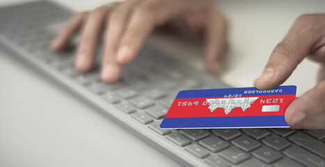 Man pays online with plastic bank card with printed flag of Cambodia. Fictional numbers