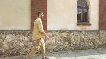 Side view of adult male traveler in yellow shirt walks along a narrow old street. Tourism during quarantine