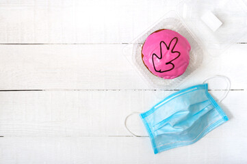 Pandemic concept, coronavirus infection outbreak, food delivery for healthcare workers. Berliner donut in a container and a medical mask on a white background. Copy space.