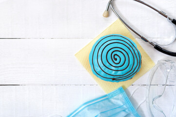 Pandemic concept, coronavirus infection outbreak, food delivery for healthcare workers. Berliner in blue glaze and health worker tools and protective equipmenton on a white wooden background.