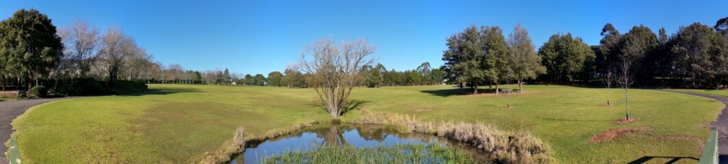 Fototapeta na wymiar Beautiful morning panoramic view of a small pond in a park with reflections of deep blue sky and tall trees, Fagan park, Galston, Sydney, New South Wales, Australia